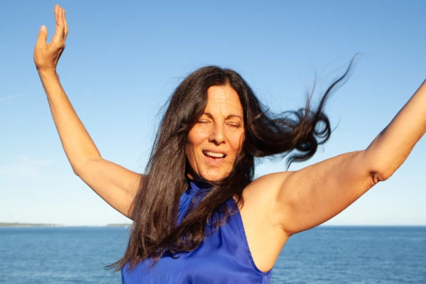 femme cheveux long, brun dans le vent, bras ouvert, ciel bleu, elle chante