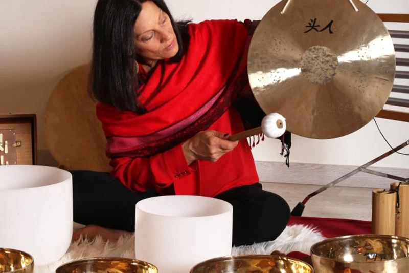 Danielle Blackman Cartau un gong à la main entourée de divers instruments vibratoires